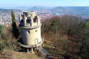 Steinerner runder Turm auf einem Gipfel; im Hintergrund Jena-Ost und das Stadtzentrum mit JenTower