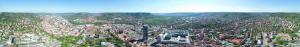 Ein breites Panorama Bild der Stadt Jena, aufgenommen aus sehr großer Höhe. Zentriert finden sich JenTower und der Campus der FSU. Im rechten Teil: Jena West. Im linken Teil: Jena Ost. Im Hintergund: Paradiespark und Jena Süd.