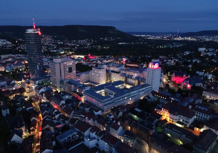 Schräges Luftbild des bei Nacht erleuchteten FSU Campus, links der JenTower.